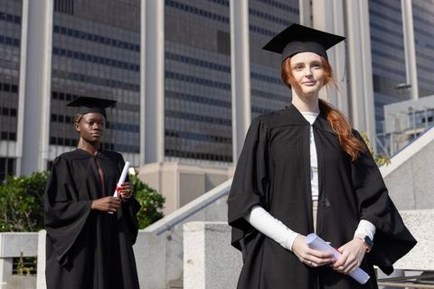 Diverse female graduates posing on urban steps holding diplomas celebrating milestone