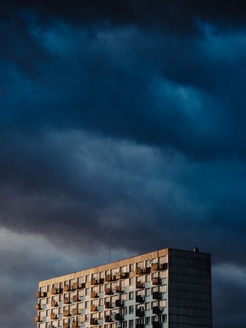 Concrete apartment building under dark, stormy sky. Great for urban lifestyle themes, weather impacts on architecture, and city residential topics.