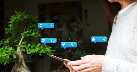 Checking social media notifications beside bonsai in modern home office