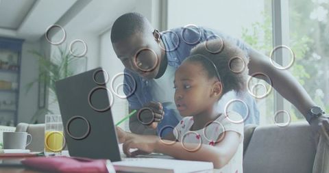 Father guiding daughter at laptop while pointing with pencil during home learning