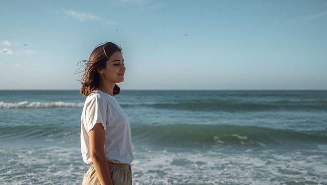 Young woman standing at shoreline enjoying calm ocean breeze and wide blue horizon