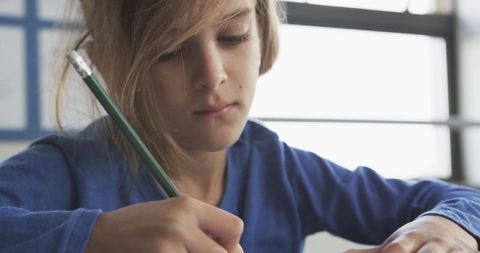 Child deep in concentration writing with pencil in bright classroom