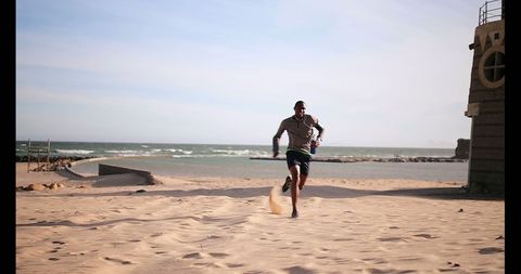 Young Man Jogging on Sunny Beach with Sea in Background