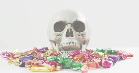 Skull surrounded by colorful wrapped candies on white high-key surface