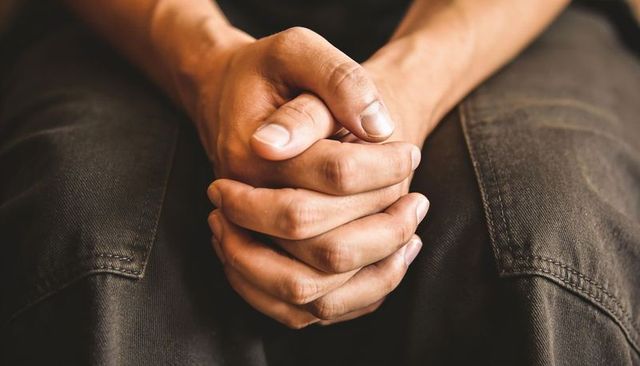 Clasped hands on lap closeup conveying contemplation and quiet strength, fabric detail