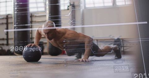 Shirtless mid-adult male performing medicine ball push-up with hud fitness data overlay