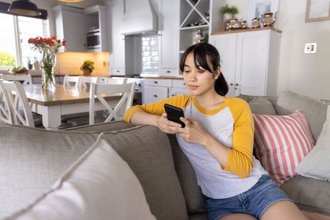 Asian woman relaxing on sofa using smartphone in modern cozy living room