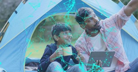 Father and son exploring augmented reality while camping in tent using tablet and mug