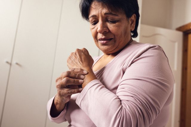 Mature woman experiencing wrist pain, touching her hand with a distressed expression. Useful for illustrating concepts related to arthritis, healthcare, joint pain, and the emotional impact of chronic illness. Ideal for medical articles, healthcare websites, and retirement planning resources.