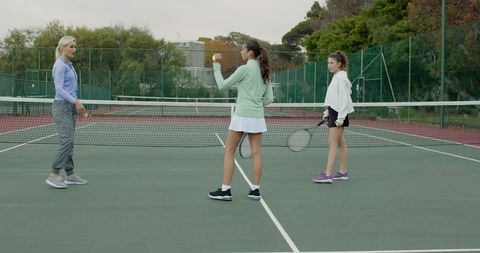 Women practicing tennis on outdoor court during coaching session trio training and teamwork