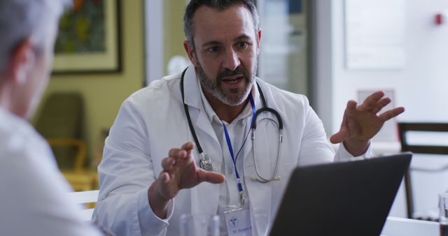 Caucasian male doctor using laptop sitting and addressing hospital colleagues at a meeting. medicine, health and healthcare services.