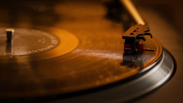 Warm close-up of spinning vinyl record with tonearm gliding and stylus tracking groove