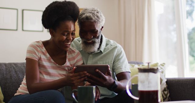 Happy african american couple sitting on couch making image call with tablet smiling and waving. staying at home in isolation during quarantine lockdown.