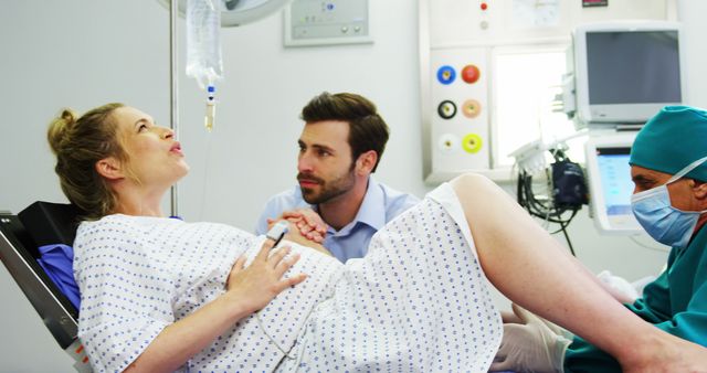 A Caucasian woman in labor experiences contractions as a supportive Caucasian man, the father, and a healthcare professional, a doctor or midwife, assist her during childbirth, with copy space. The intensity of the moment is captured as they focus on the delivery process in a medical setting.