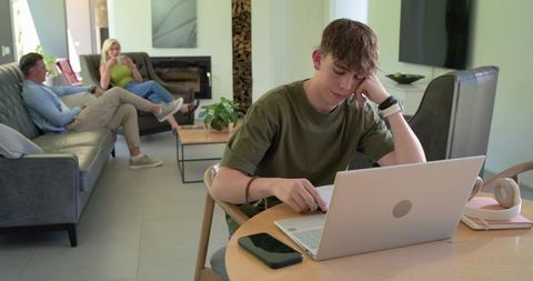 Teenager studying on laptop while parents relaxing in modern minimalist living room