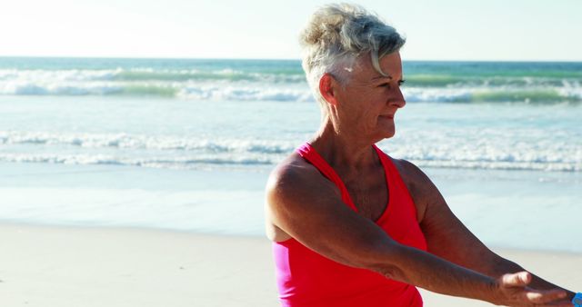 Senior woman in sportswear exercising on a beach near ocean waves, enjoying active and healthy lifestyle. Ideal for representing wellness, fitness, leisure, and senior health activities. Can be used in health and fitness promotions, senior living advertisements, wellness articles, and travel brochures emphasizing outdoor activities.