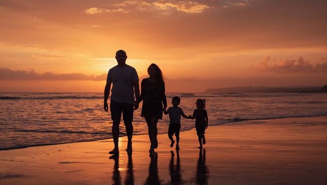Silhouetted family walking hand in hand on sunset beach with reflective ocean glow