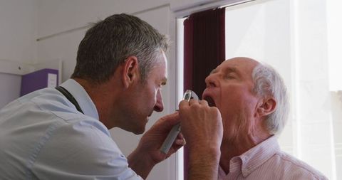 Doctor examining senior mans throat at clinic visit
