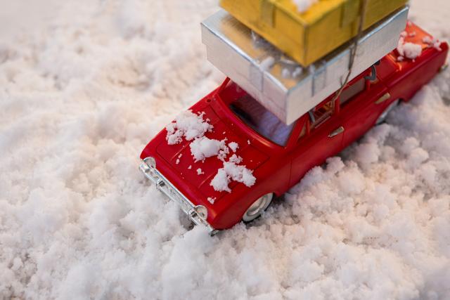 Red toy car carrying stack of Christmas presents on snow, evoking festive holiday spirit. Ideal for holiday promotions, Christmas cards, winter-themed designs, and gift shop advertisements.