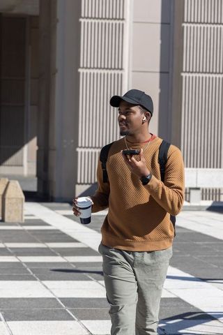 African American Man Walking in Urban Plaza Talking on Smartphone Holding Coffee Cup