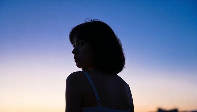 Gazing asian woman silhouetted at twilight on rooftop with bob haircut and thin straps