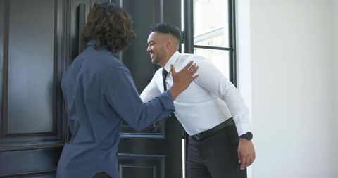 African colleagues greeting at front door leaning in for warm hug and handshake