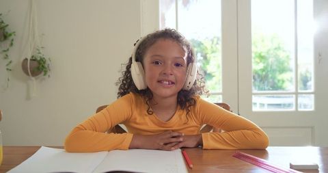 Smiling girl wearing headphones studying at home desk with notebook pencil ruler