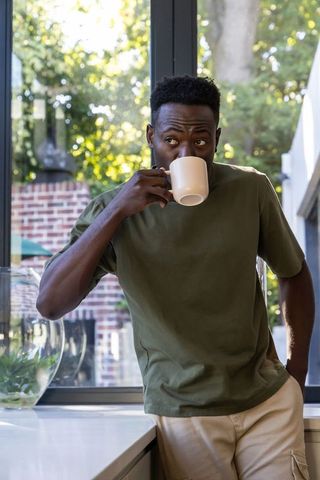 African american man sipping coffee at kitchen counter by sunlit window, cozy morning