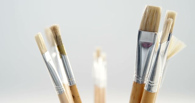 Close-up view of a variety of artist paintbrushes with wooden handles against a light blue background. Ideal for use in art-related content, creative workshops, DIY tutorials, or supply store promotions.