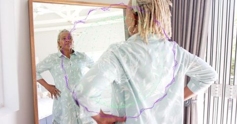 Mature woman inspecting and adjusting dress in mirror with augmented reality overlay