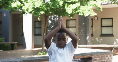 African american boy practicing mindful meditation outdoors in sunny courtyard