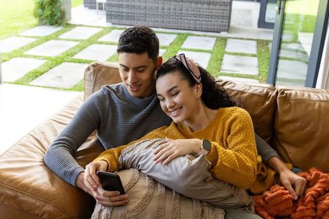 Young couple relaxing on sofa at home sharing smartphone and cozy weekend moments