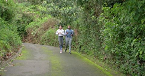 Couple jogging on mossy rural lane surrounded by lush green hedges