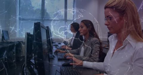 Businesswomen collaborating at desktops with digital globe network overlay for training