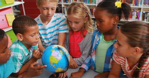 Elementary students exploring globe together in diverse classroom library