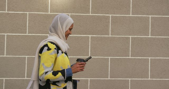 Woman in Headscarf Checking Phone While Walking with Coffee - Download Free Stock Images Pikwizard.com