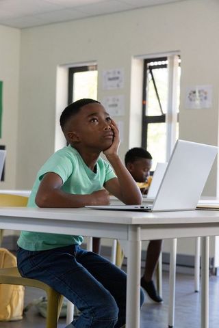 African american boy daydreaming at laptop in classroom during digital learning
