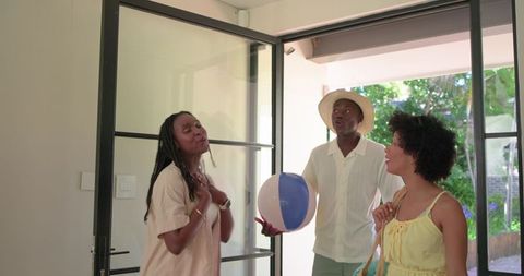 African american friends entering home carrying beach ball and summer tote, smiling
