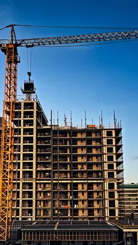 Tower crane operating over high-rise construction site during golden hour vertical video