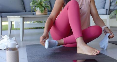 African american woman putting on socks on yoga mat on covered patio for active wellness
