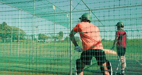 Cricket batting practice in outdoor net cage, indian man coaching teenage teammate