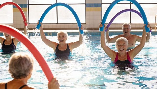 Active seniors enjoying water aerobics with colorful foam noodles in indoor community pool