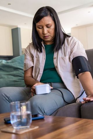 Mature woman measuring blood pressure at home with upper-arm cuff and digital monitor