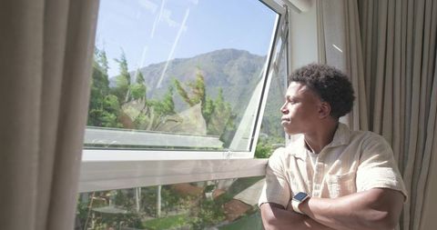 Man leaning at open window gazing at mountain view in warm sunlight for contemplation