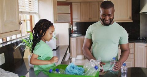 Father and daughter recycling plastic bottles in kitchen