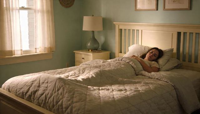 Serene woman sleeping in sunlit bedroom with quilted comforter and wooden headboard