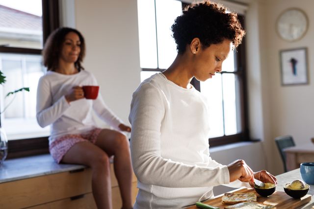Diverse lesbian couple drinking coffee and preparing breakfast in kitchen - Download Free Stock Photos Pikwizard.com
