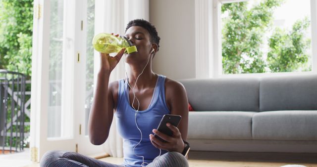 African american woman drinking water and using smartphone at home. lifestyle living during self isolating in quarantine lockdown