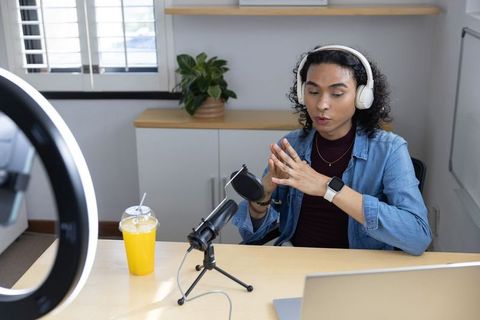 Nonbinary creator recording podcast in home studio with headphones, microphone, ring light