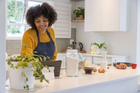 Smiling woman following recipe on tablet while baking at bright modern kitchen island